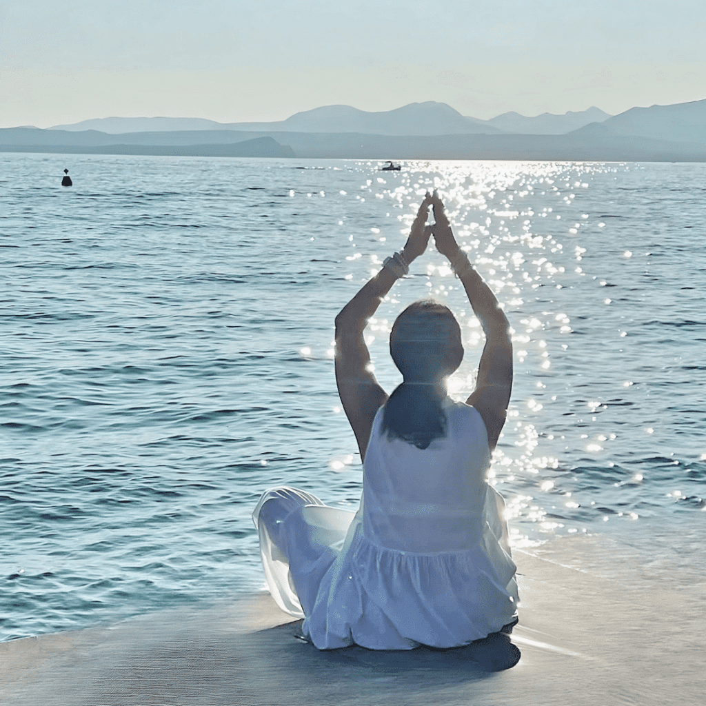 Frau meditiert am Meer bei Sonnenuntergang.