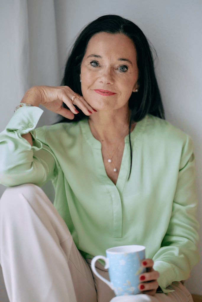 Frau hält Tasse in heller Kleidung.