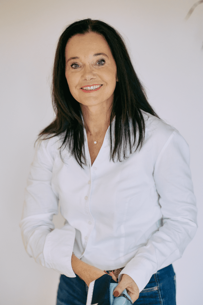 Lächelnde Frau in weißer Bluse und Jeans.